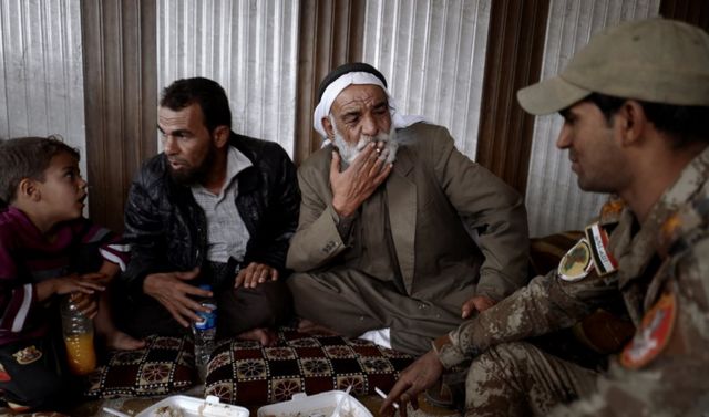 مجموعة من المدنيين يجلسون ويأكلون ويدخنون مع جنود الفرقة الذهبية