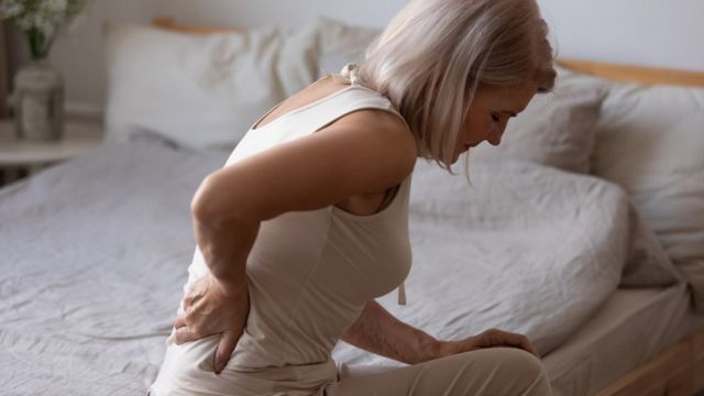 Una mujer sentada en la cama con dolor de espalda