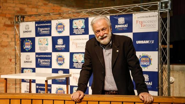 Tonucci sorrindo em frente a painel de evento em Jundiaí