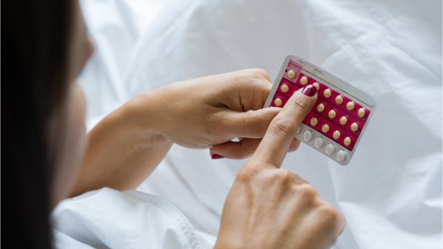 Mulher observa cartela com pílulas anticoncepcionais