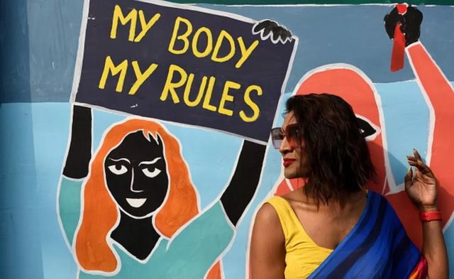 Mulher ao lado de grafite com a mensagem: "meu corpo, minhas regras"