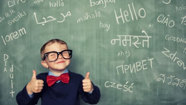 Niño frente a una pizarra con palabras en varios idiomas.