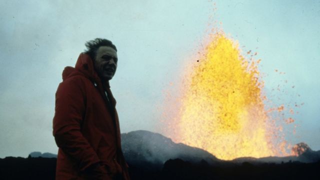 Hombre cubierto con chaqueta roja al lado de una fuente de lava