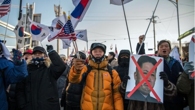 Protestors holding US and South Korean flags, and a sign with Kim Jong-Un's face crossed out.