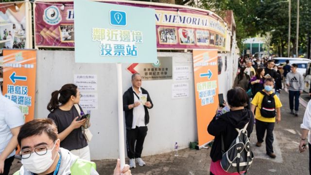 香港新界上水一处“邻近边境投票站”外工作人员举起指示牌引导选民进场（中新社图片10/12/2023）