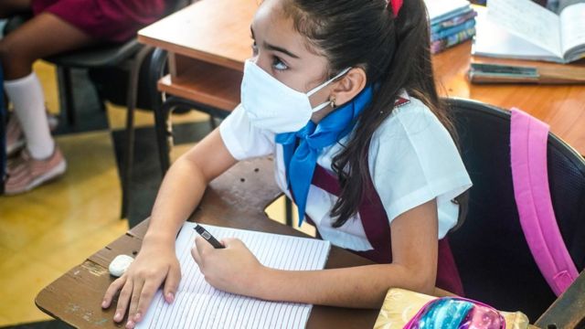 Niña con mascarilla sentada en un pupitre en una escuela en Cuba