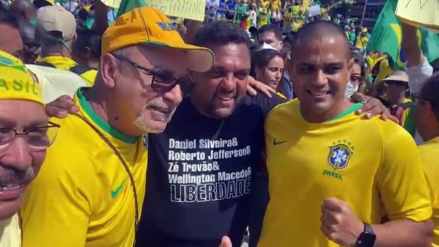 Queiroz posa para foto ao lado de manifestantes, um deles com camisa preta que diz: Daniel Silveira & Roberto Jefferson & Zé Trovão & Wellington Macedo & LIBERDADE