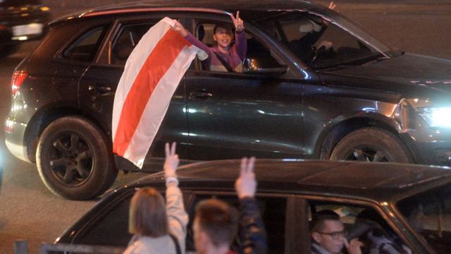 Люди в машине с бело-красно-белым флагом в Минске 23 сентября