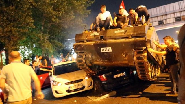 Turkish men sitting on a tank as it runs over cars, Istanbul, Turkey, July 2016