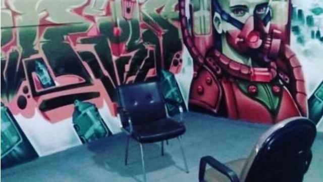 Espaço de atendimento da PerifAnálise no centro cultural Favela Galeria. A foto mostra duas cadeiras de escritório, uma em frente à outra, com uma parede grafitada ao fundo