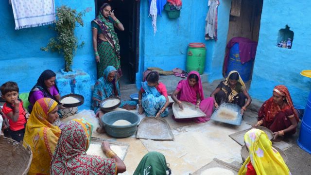 Mujeres preparan comida en el piso de un patio.