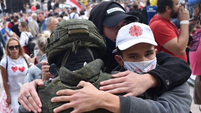 People hug a Belarus law enforcement officer during a protest rally