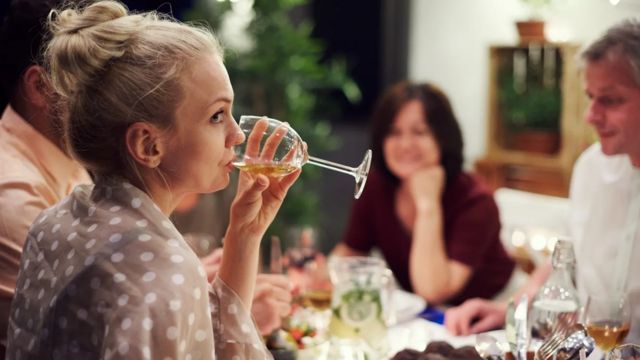 Mujer bebiendo vino en una cena.