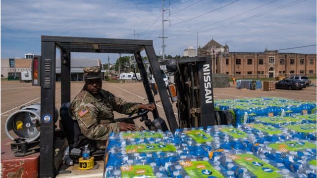 Militar dos EUA conduz empilhadeira carregada com garrafas de água mineral