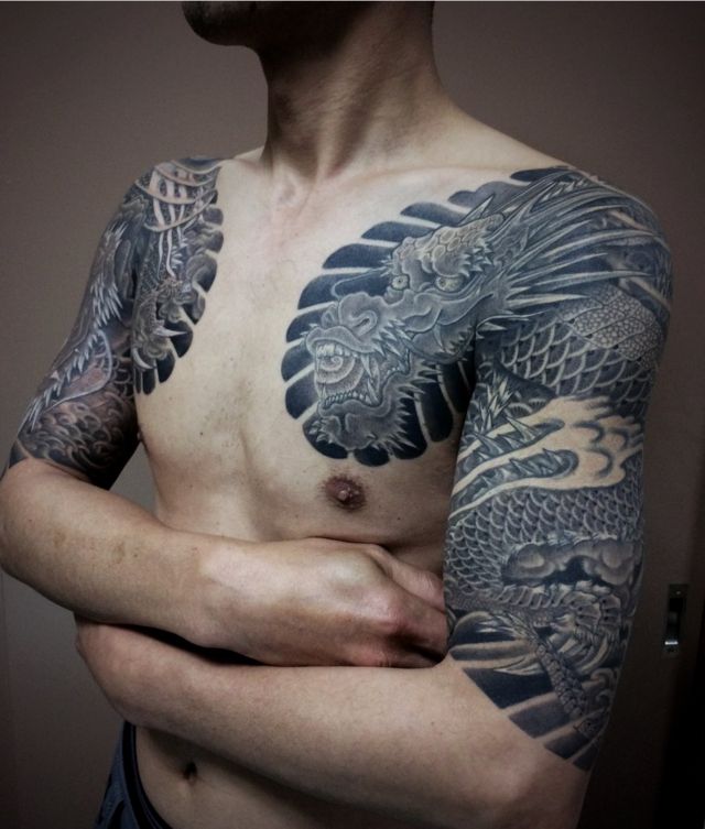 A man displays dragon tattoos on his upper arms and chest