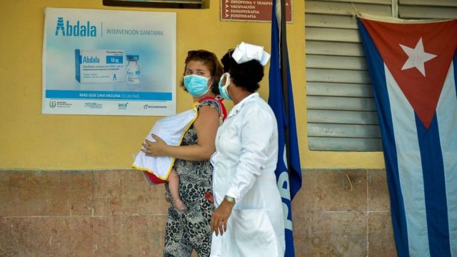 Mulher cubana com bebê ao lado de enfermeira em posto de vacinação em Cuba