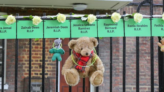 Osos de peluche colgados de una reja con carteles de los nombres de niños que murieron en la tragedia de Grenfell