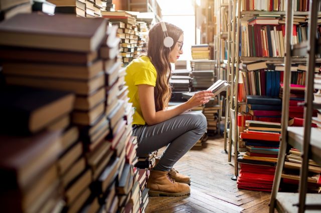 A young woman listening to an audio book, sitting on a pile of books