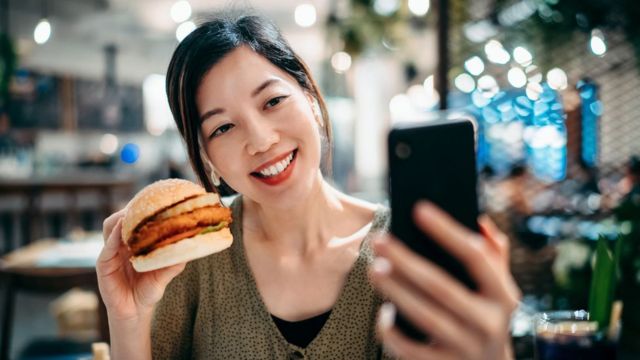 Mulher fazendo selfie com hamburguer