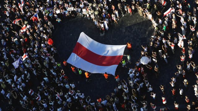A large historical white-red-white flag of Belarus is pictured inside a heart formed by demonstrators