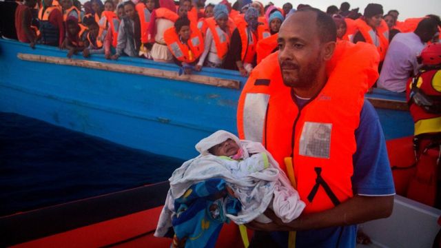 Un homme porte son fils âgé de cinq jours sur l'une des embarcations de sauvetage.