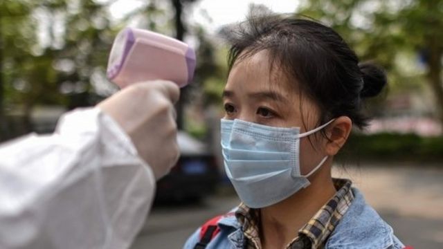 A man wearing a protective suit checks a woman's temperature next to a residential area in Wuhan, in China"s central Hubei province on April 7, 2020.