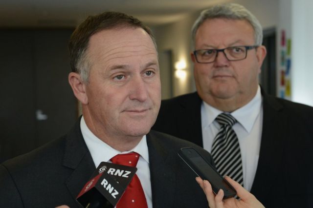 New Zealand Prime Minister John Key speaks to the media while Earthquake Recovery Minister Gerry Brownlee looks on ahead of a Civic Memorial Service held in the Botanical Gardens for victims of the 2011 Christchurch Earthquakes on 22 February 2016 in Christchurch, New Zealand