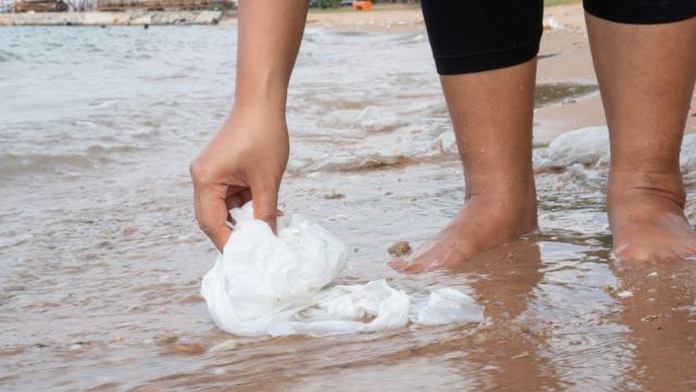 Pessoa com os pés em ná agua retirando lixo da beirada do rio