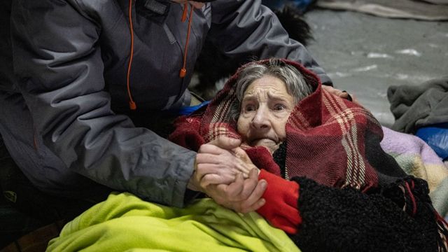 An elderly woman is helped to cross an improvised path along a destroyed bridge to flee the city of Irpin, Ukraine, on 8 March 2022