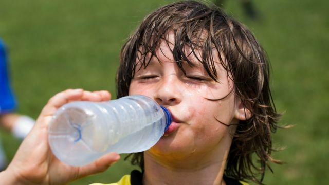 Un niño bebe agua de una botella.