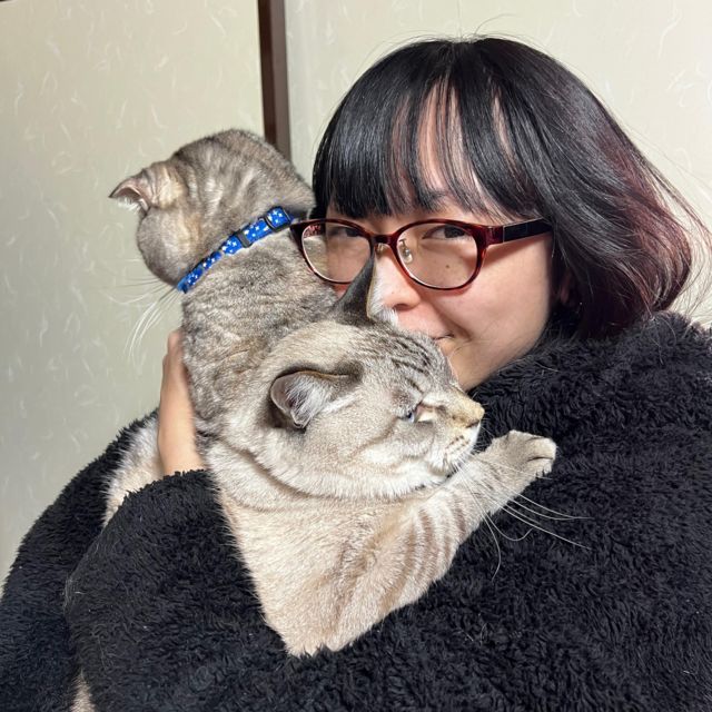 Jovem japonesa segura dois gatos cinzas no colo