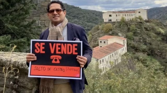 Ronnie Rodríguez of the investment firm representing the owner of the village poses with the 'for sale' sign