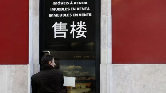 Fotografia de letras em fachada dizendo "imóveis à venda" em diversos idiomas, incluindo em caracteres chineses