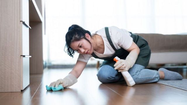 Mulher limpando o chão da casa de luva usando desinfetante