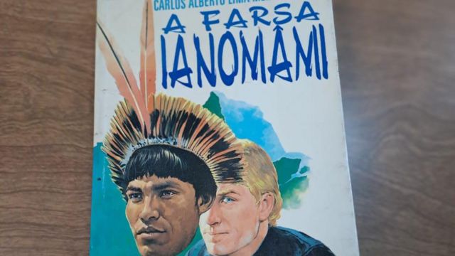 Capa do livro mostra homem loiro de olhos azuis segurando máscara com feições indígenas