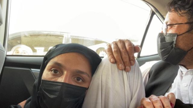 Zarifa Ghafari, usando um lenço que cobre o rosto, se esconde em um carro