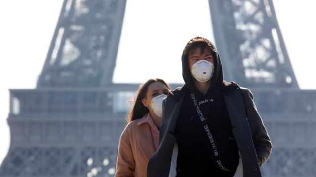 A young couple of tourists with protective masks against coronavirus are walking on the Trocadero esplanade in front of the Eiffel Tower. After buying statuettes, the couple wash their hands with a hydroalcholic solution in Paris, France, March 7, 2020
