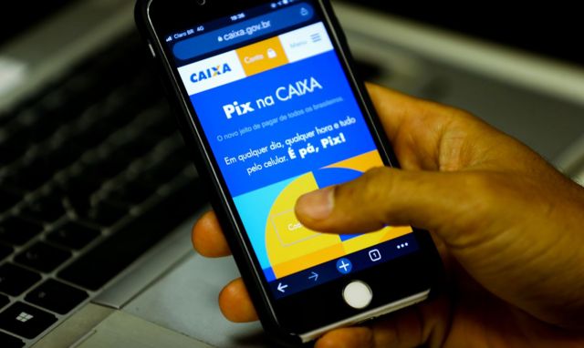 Mão segurando celular com imagem sobre uso do Pix na Caixa Econômica Federal