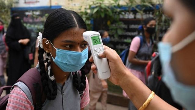 Una maestra en India le toma la temperatura a una de sus alumnas.