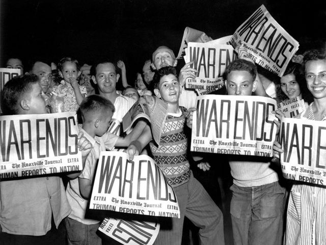 Children hold newspapers declaring the end of World War Two