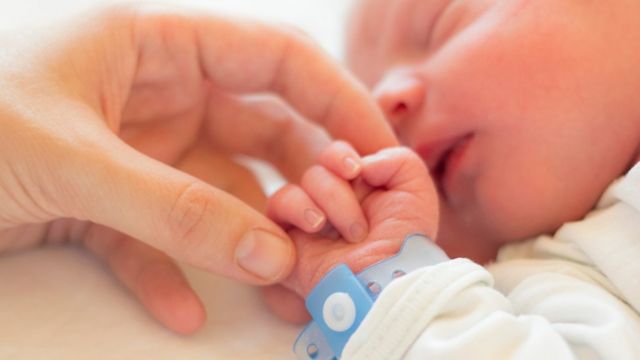 Mano de un adulto sosteniendo la mano de un bebé recién nacido