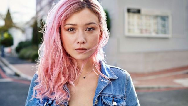 young woman with pink hair and denim jacket alone