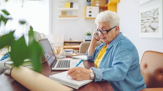 Idosa trabalhando no computador e telefone