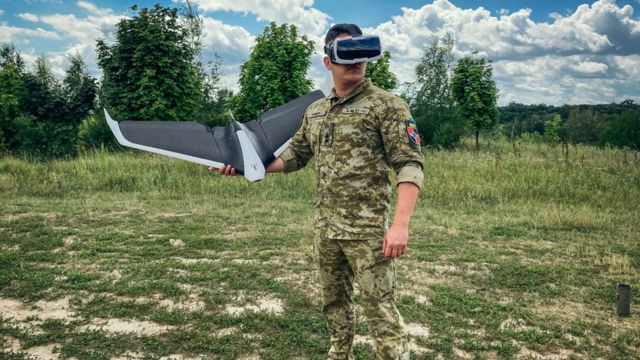 A Ukrainian soldier wearing virtual reality goggles prepares to launch a "Parrot" drone in a field