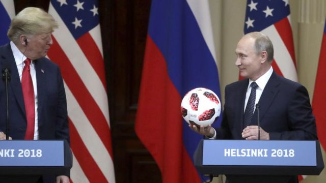 Путин держит мяч с улыбкой, Трамп смотрит на него вопросительно