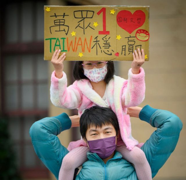 一名妇女举起女儿，她的女儿举着支持台湾民众党的标语牌