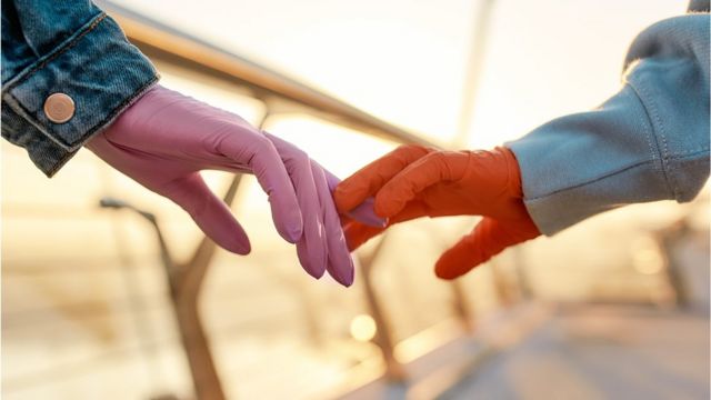 A couple walks hand in hand, but one of the persons is wearing protective gloves