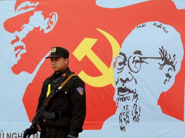 Người lính bên cạnh biểu tượng búa liềm và hình ảnh Hồ Chí Minh
