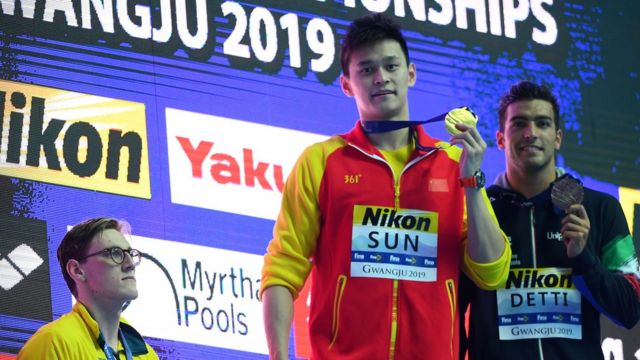 Silver medalist Mack Horton of Australia (L) watches as gold medalist Sun Yang of China hold up his medal, with bronze medalist Gabriele Detti of Italy (R) during the medal ceremony for Men"s 400m Freestyle Final on day one of the Gwangju 2019 FINA World Championships at Nambu International Aquatics Centre on July 21, 2019 in Gwangju, South Korea.