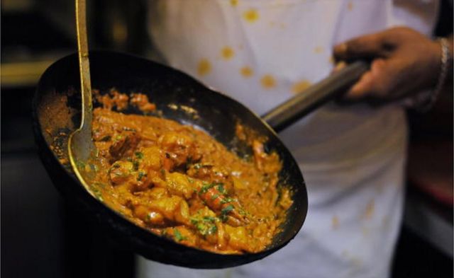 A chef prepares a curry dish in an Indian restaurant kitchen